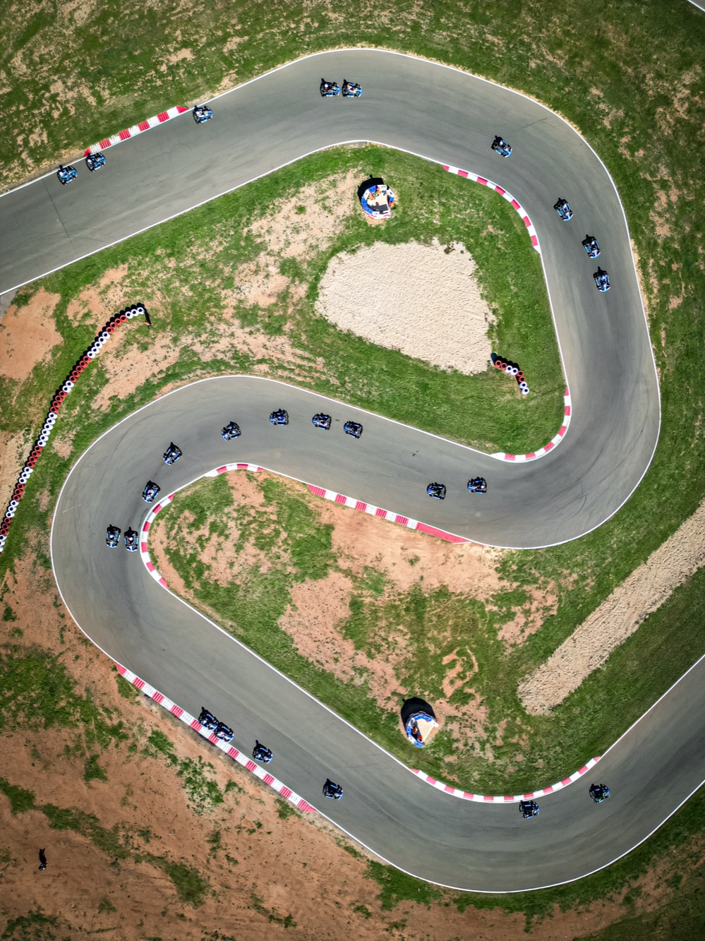 Aerial view of a kart circuit with a field of karts strung through the esses between red-and-white kerbs